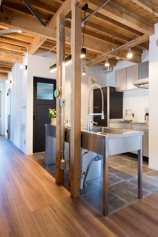 Cette photo montre une cuisine ouverte parallèle industrielle avec un évier 1 bac, un placard à porte plane, des portes de placard grises, un plan de travail en inox, îlot et un sol gris.