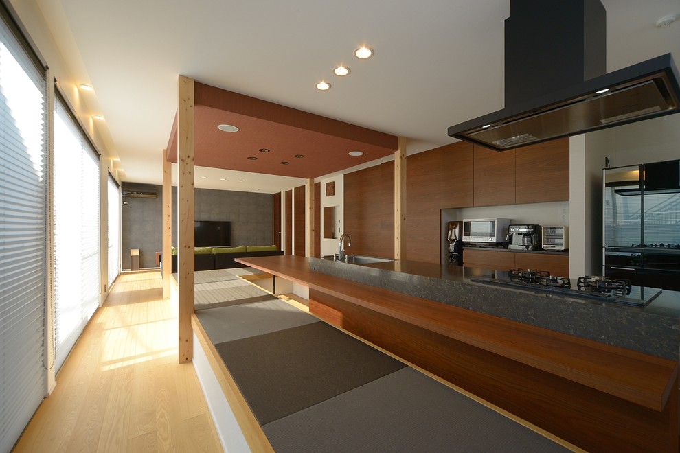 Foto de cocina asiática grande abierta con armarios con paneles lisos, puertas de armario de madera en tonos medios, electrodomésticos negros y suelo de madera clara
