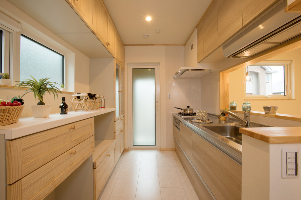 Inredning av ett asiatiskt linjärt kök med öppen planlösning, med en enkel diskho, luckor med infälld panel, skåp i ljust trä, bänkskiva i rostfritt stål, vitt stänkskydd, en halv köksö och beiget golv