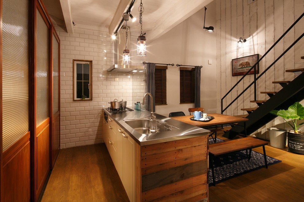 Cette photo montre une cuisine américaine linéaire rétro en bois brun avec un évier intégré, un plan de travail en inox, une péninsule, un placard à porte plane, un électroménager en acier inoxydable et un sol en bois brun.