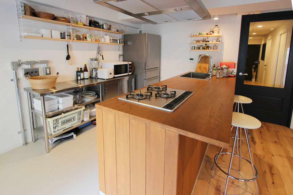 Cette photo montre une cuisine ouverte linéaire industrielle avec un évier 1 bac, un plan de travail en bois, une péninsule et un sol beige.