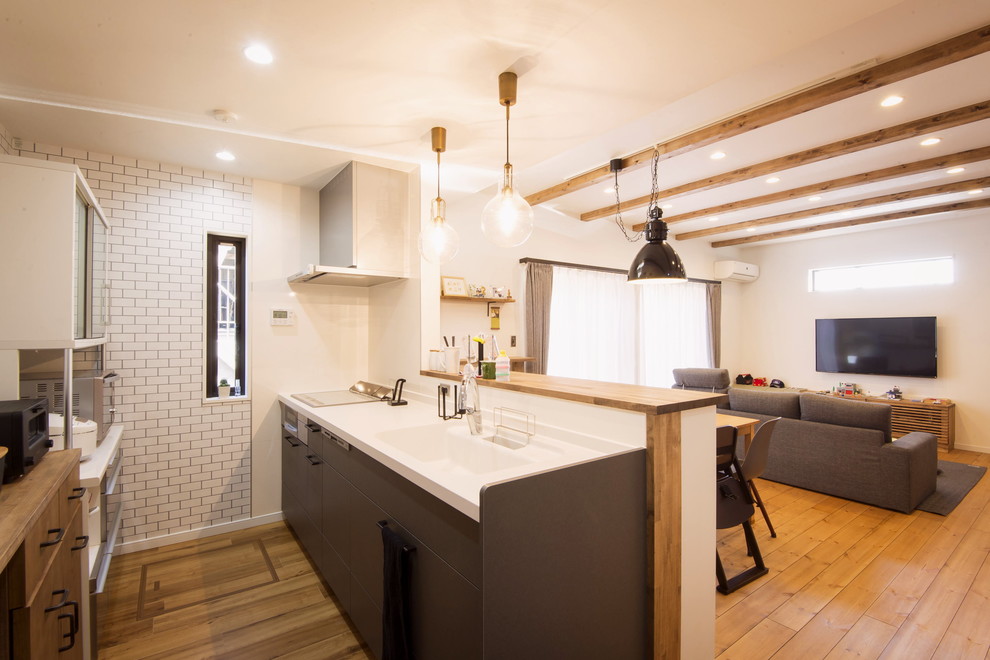 На фото: кухня-гостиная среднего размера в стиле кантри с паркетным полом среднего тона, коричневым полом, монолитной мойкой, плоскими фасадами, черными фасадами, полуостровом и коричневой столешницей