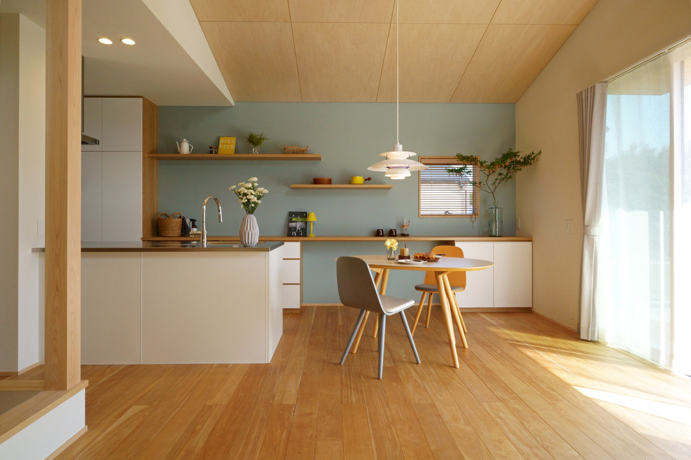 Inspiration för ett minimalistiskt brun brunt kök, med en integrerad diskho, släta luckor, vita skåp, bänkskiva i rostfritt stål, mellanmörkt trägolv, en halv köksö och brunt golv