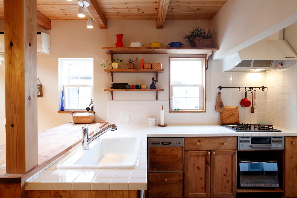 Exempel på ett lantligt l-kök, med en nedsänkt diskho, luckor med infälld panel, skåp i mellenmörkt trä, kaklad bänkskiva, vitt stänkskydd, stänkskydd i keramik och en halv köksö