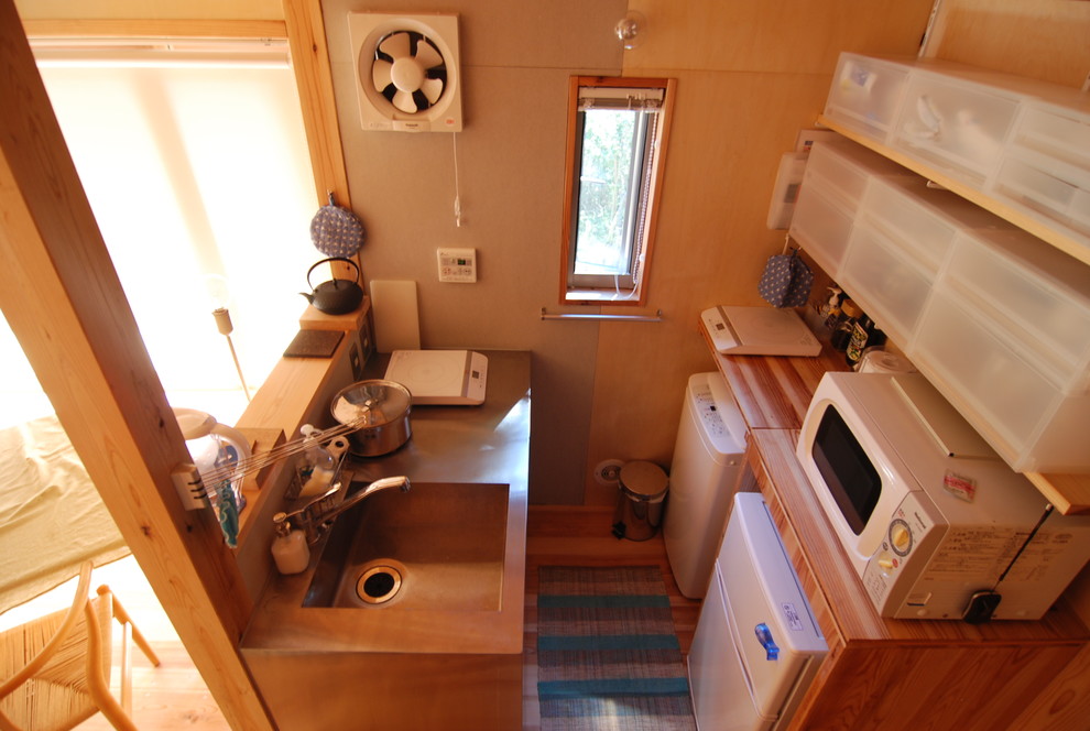 Immagine di una piccola cucina stile rurale con lavello integrato, ante lisce, ante in acciaio inossidabile, top in acciaio inossidabile, elettrodomestici bianchi, pavimento in compensato e penisola