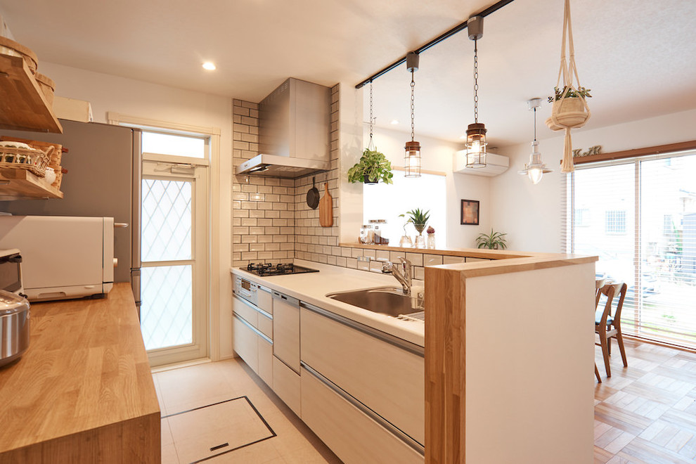 Exempel på ett minimalistiskt kök med öppen planlösning, med en enkel diskho, släta luckor, beige skåp, vitt stänkskydd, stänkskydd i tunnelbanekakel och beiget golv