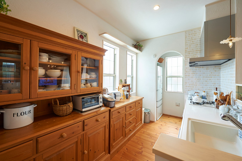 Modelo de cocina lineal de estilo de casa de campo abierta con fregadero integrado, armarios con paneles lisos, salpicadero beige, electrodomésticos blancos y suelo de madera clara