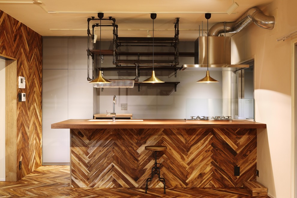 Einzeilige Industrial Küche mit Arbeitsplatte aus Holz, braunem Holzboden, Glasrückwand, Unterbauwaschbecken und Kücheninsel in Tokio
