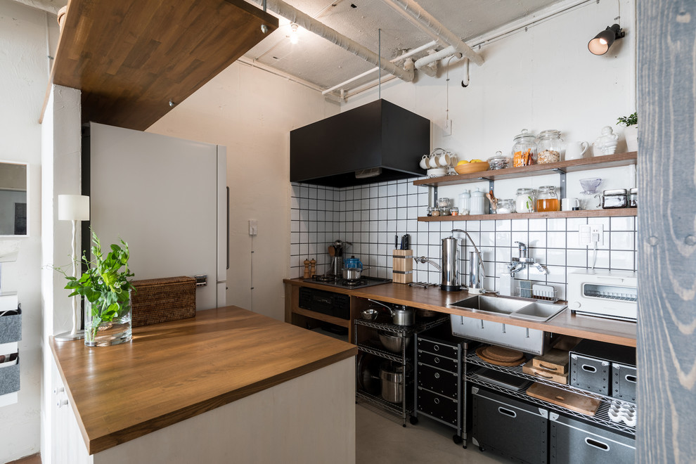 他の地域にあるコンテンポラリースタイルのおしゃれなキッチン (シングルシンク、木材カウンター、白いキッチンパネル、サブウェイタイルのキッチンパネル、グレーの床) の写真