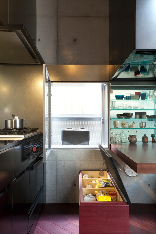 Diseño de cocina lineal urbana abierta con armarios con paneles lisos, puertas de armario negras, salpicadero metalizado, suelo de madera oscura y electrodomésticos negros