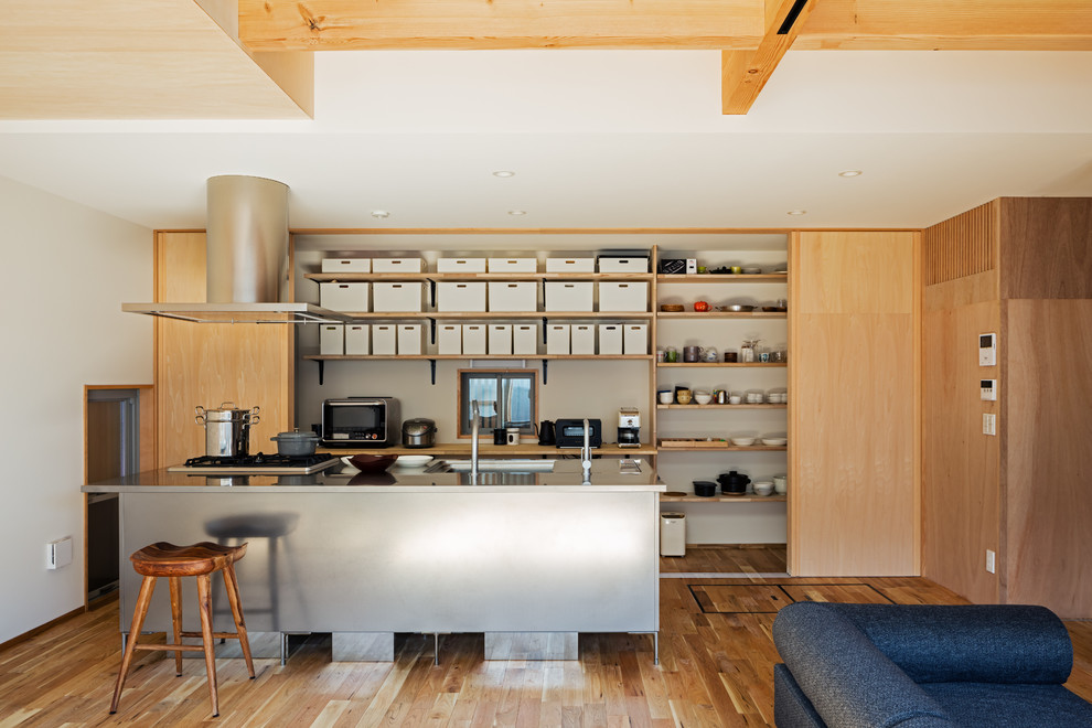 Foto på ett funkis kök, med en enkel diskho, bänkskiva i rostfritt stål, mellanmörkt trägolv, en köksö och brunt golv