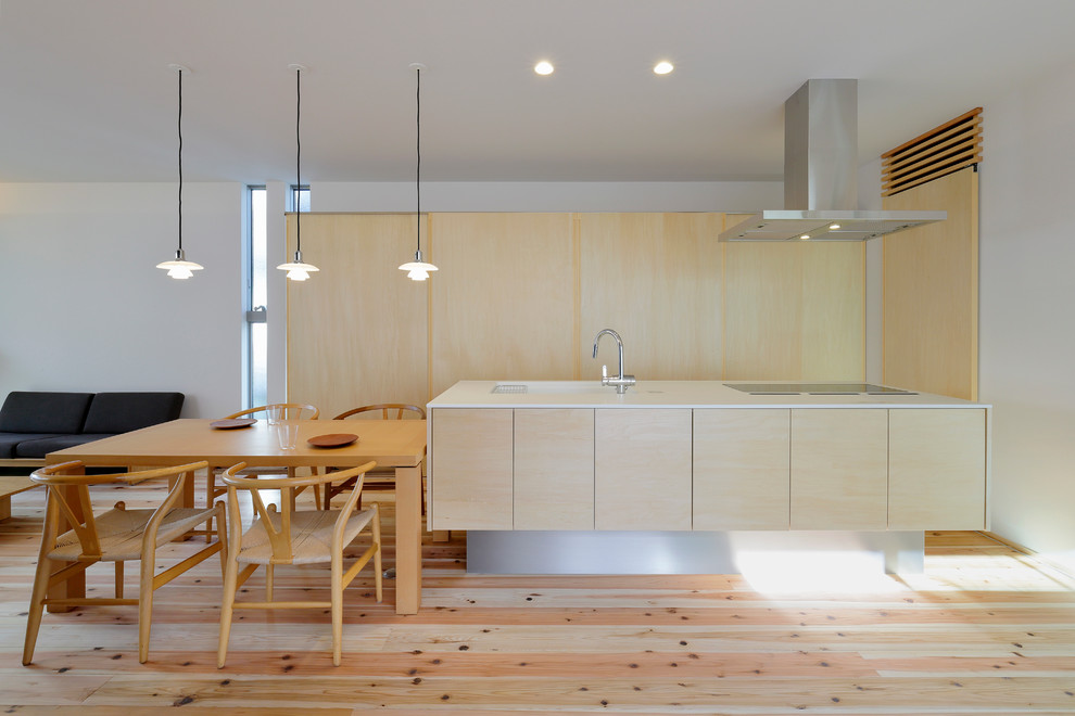 Cette image montre une cuisine ouverte parallèle asiatique en bois clair avec un évier encastré, un placard à porte plane, parquet clair, îlot, un sol beige et un plan de travail blanc.