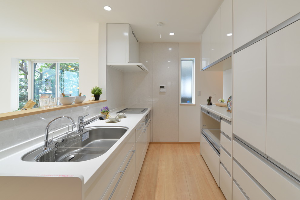 Exemple d'une cuisine ouverte linéaire moderne avec un évier 3 bacs, un plan de travail en surface solide, une crédence blanche, un électroménager blanc, parquet clair, un sol beige et un plan de travail blanc.