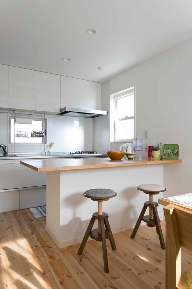 Idées déco pour une cuisine ouverte parallèle moderne avec un évier 1 bac, un placard à porte plane, des portes de placard blanches, un plan de travail en inox, un sol en bois brun, îlot et un sol marron.