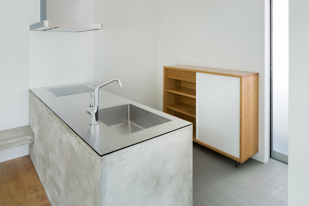 Exemple d'une petite cuisine parallèle moderne avec des portes de placard blanches, un plan de travail en inox, un évier intégré, un placard sans porte, une crédence grise et un sol en bois brun.