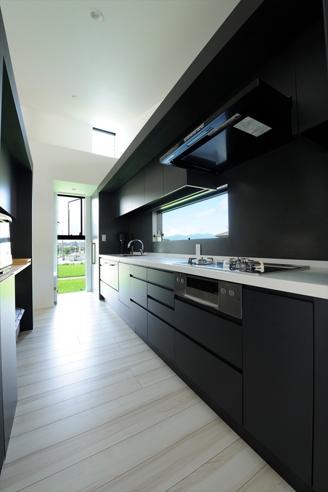Example of a large minimalist beige floor enclosed kitchen design in Other with black cabinets, solid surface countertops, black backsplash, stainless steel appliances, an island, white countertops, a single-bowl sink and flat-panel cabinets
