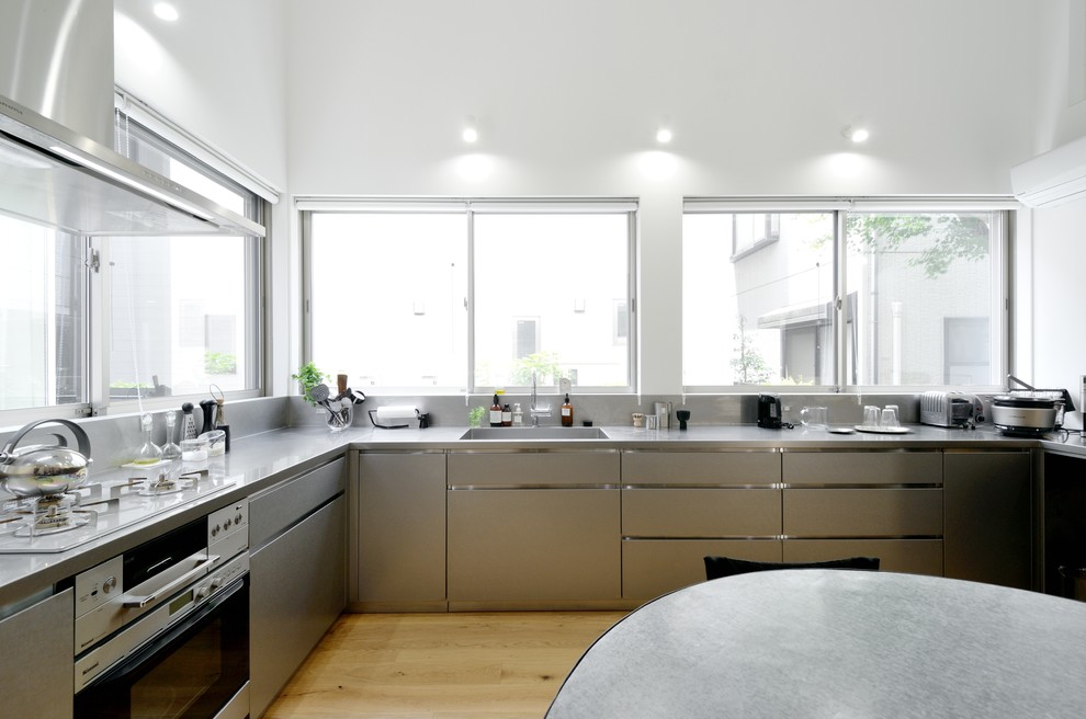 Bild på ett funkis grå grått kök, med en undermonterad diskho, skåp i rostfritt stål, bänkskiva i rostfritt stål, stänkskydd med metallisk yta, stänkskydd i metallkakel, rostfria vitvaror, ljust trägolv och vitt golv