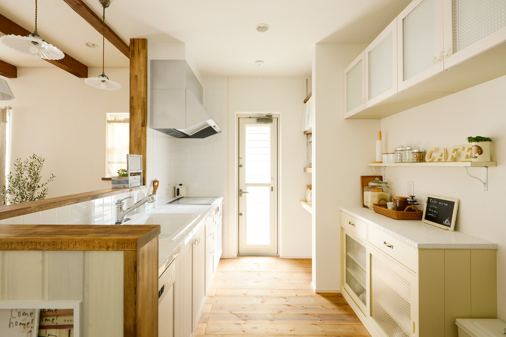 Inspiration for a small country galley kitchen in Other with a built-in sink, glass-front cabinets, white cabinets, white splashback, light hardwood flooring, a breakfast bar and white appliances.