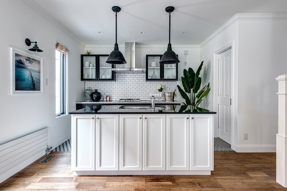 他の地域にあるトランジショナルスタイルのおしゃれなキッチン (シングルシンク、落し込みパネル扉のキャビネット、白いキッチンパネル、無垢フローリング、茶色い床) の写真