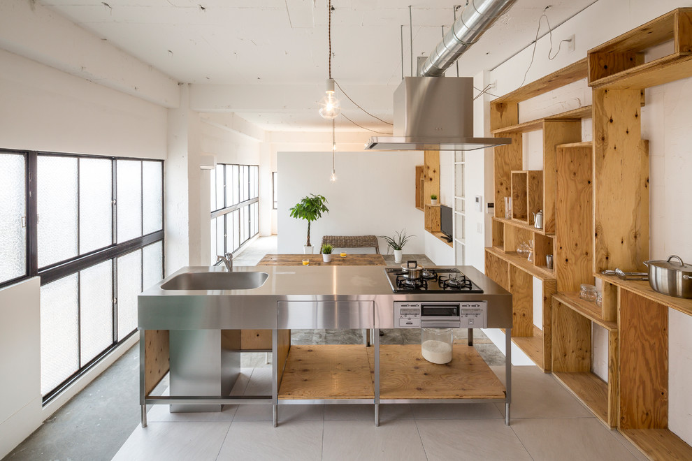 Cette photo montre une cuisine linéaire industrielle en inox avec un évier intégré, un placard à porte affleurante, un plan de travail en inox, îlot et un sol gris.