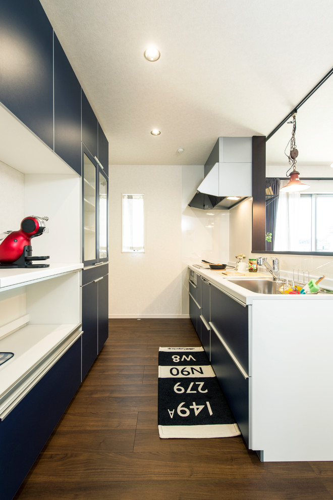 Zweizeilige Moderne Küche mit Waschbecken, flächenbündigen Schrankfronten, türkisfarbenen Schränken, dunklem Holzboden, Kücheninsel und braunem Boden in Sonstige
