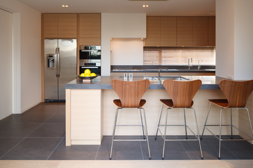 Inspiration for a large contemporary galley kitchen in Other with a double-bowl sink, flat-panel cabinets, medium wood cabinets, window splashback, porcelain flooring, a breakfast bar, grey floors and grey worktops.