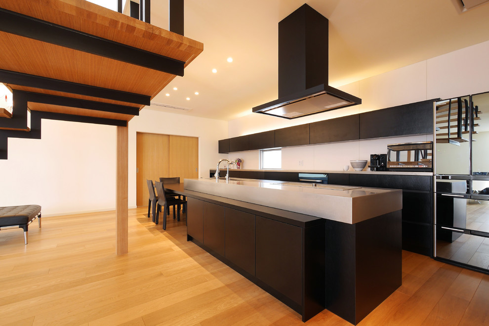 Idées déco pour une cuisine ouverte linéaire moderne avec un placard à porte plane, un sol en bois brun, îlot, des portes de placard noires et un plan de travail en inox.