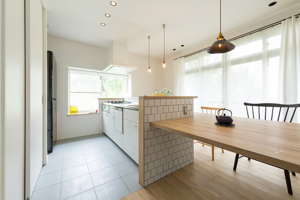 他の地域にある北欧スタイルのおしゃれなI型キッチン (フラットパネル扉のキャビネット、白いキャビネット、ステンレスカウンター、淡色無垢フローリング、茶色い床) の写真