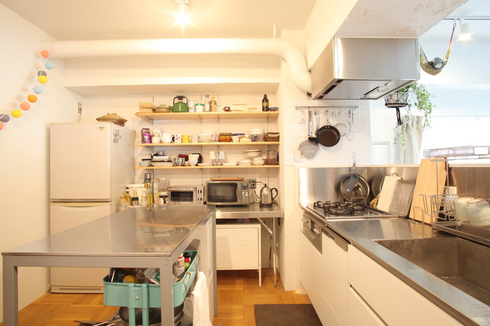 東京23区にあるアジアンスタイルのおしゃれなキッチン (シングルシンク、フラットパネル扉のキャビネット、白いキャビネット、ステンレスカウンター、メタリックのキッチンパネル、無垢フローリング、茶色い床) の写真