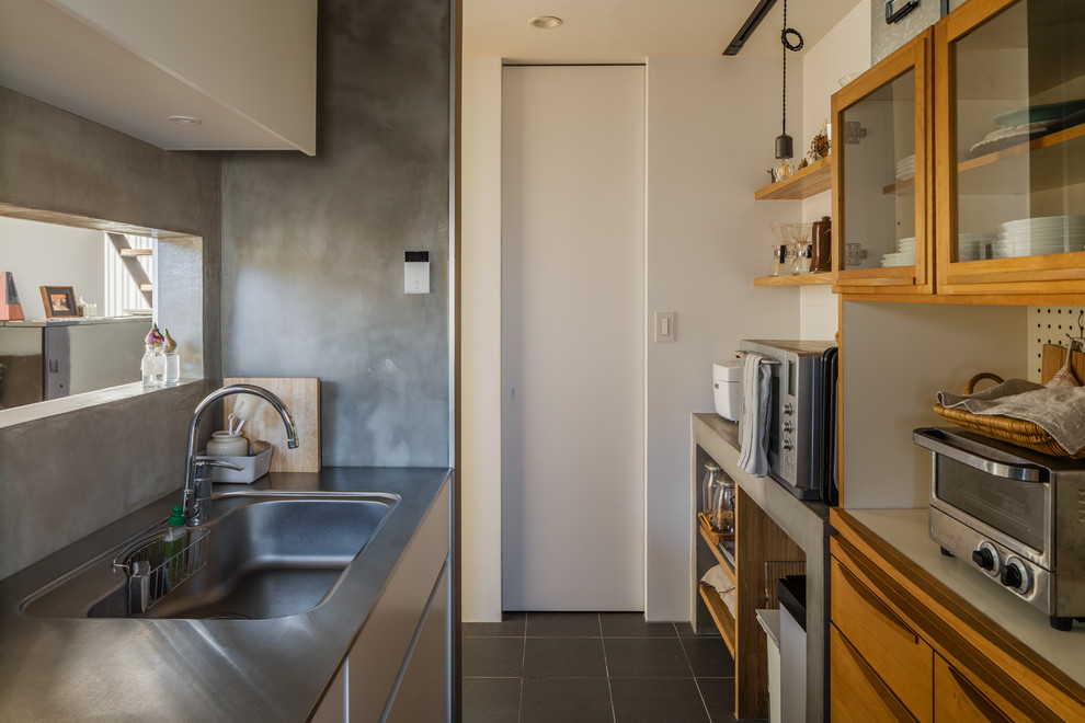 World-inspired galley kitchen in Other with an integrated sink, flat-panel cabinets, medium wood cabinets, stainless steel worktops, white splashback, stainless steel appliances, grey floors and grey worktops.