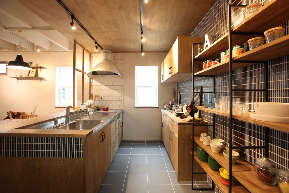 Idéer för industriella linjära kök med öppen planlösning, med en integrerad diskho, släta luckor, skåp i mellenmörkt trä, bänkskiva i rostfritt stål, svart stänkskydd, stänkskydd i stickkakel, en köksö och grått golv