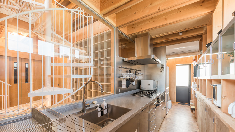 Foto på ett industriellt kök, med en enkel diskho, släta luckor, grått stänkskydd, ljust trägolv och en köksö