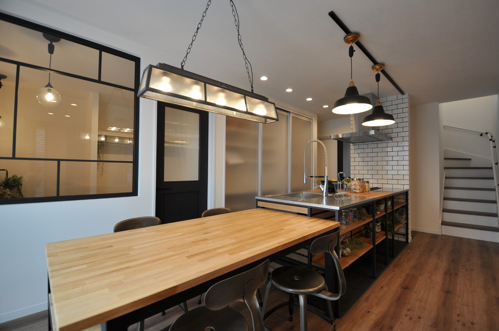 他の地域にあるインダストリアルスタイルのおしゃれなキッチン (シングルシンク、ステンレスカウンター、塗装フローリング、茶色い床) の写真
