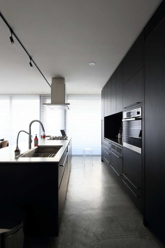 Idéer för ett modernt kök med öppen planlösning, med en undermonterad diskho, släta luckor, svarta skåp, bänkskiva i rostfritt stål, rostfria vitvaror, betonggolv och en köksö