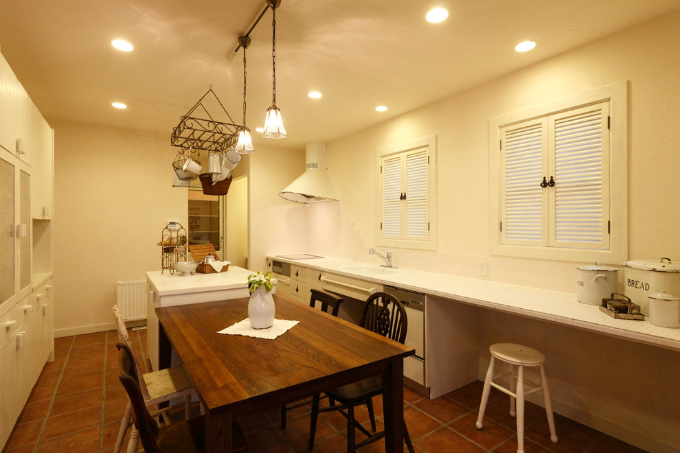 他の地域にあるシャビーシック調のおしゃれなキッチン (一体型シンク、フラットパネル扉のキャビネット、ベージュのキャビネット、テラコッタタイルの床、茶色い床、白いキッチンカウンター) の写真