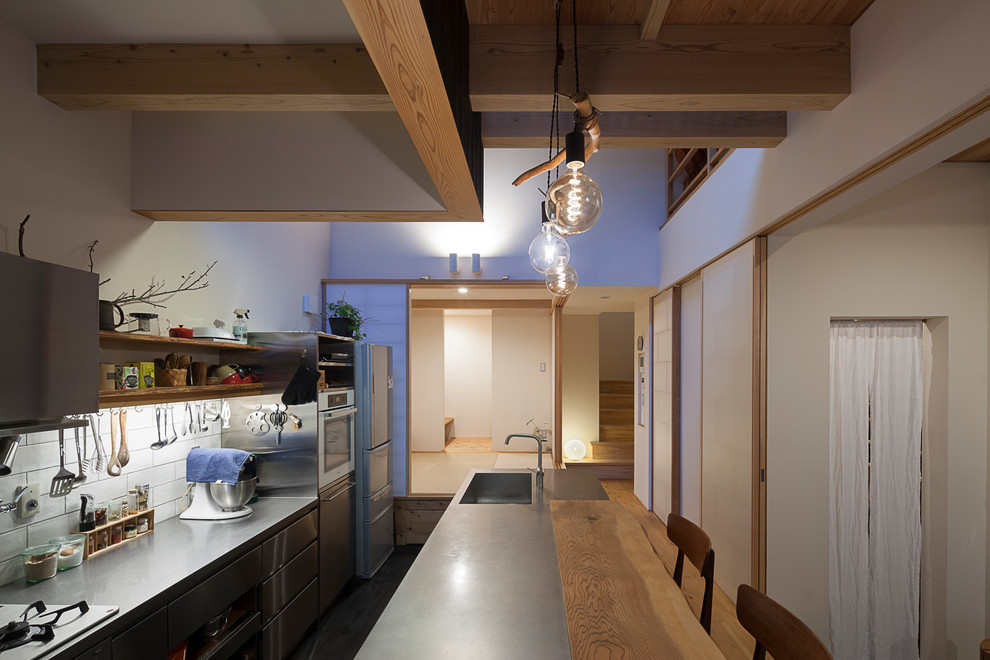 Inredning av ett modernt kök, med en integrerad diskho, öppna hyllor, skåp i rostfritt stål, bänkskiva i rostfritt stål, vitt stänkskydd, stänkskydd i porslinskakel, rostfria vitvaror, mörkt trägolv, en köksö och svart golv