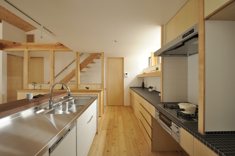 他の地域にある北欧スタイルのおしゃれなキッチン (一体型シンク、フラットパネル扉のキャビネット、ステンレスカウンター、無垢フローリング、茶色い床、黒いキッチンカウンター) の写真