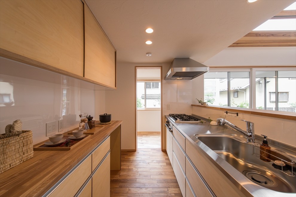 東京23区にあるアジアンスタイルのおしゃれなキッチン (シングルシンク、フラットパネル扉のキャビネット、淡色木目調キャビネット、ステンレスカウンター、白いキッチンパネル、無垢フローリング、茶色い床、茶色いキッチンカウンター) の写真