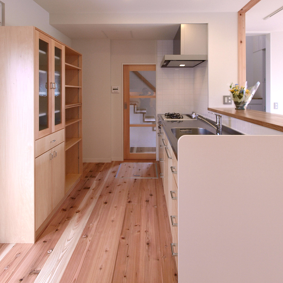 Foto di una cucina lineare nordica con top in acciaio inossidabile, parquet chiaro, lavello integrato, ante lisce, ante in legno chiaro, penisola, pavimento marrone e top marrone