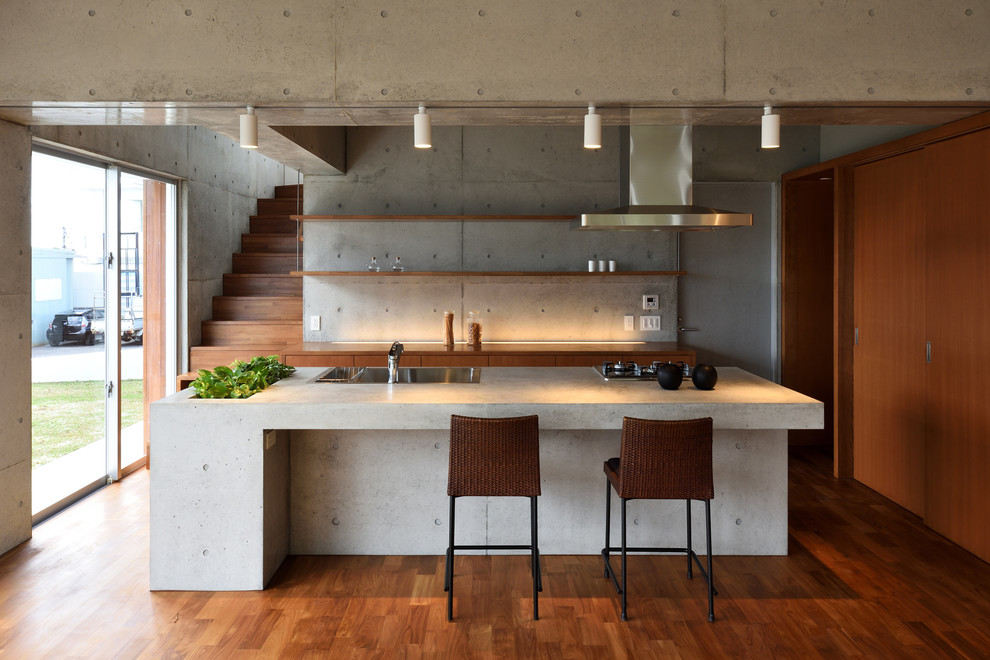 Foto di una cucina minimalista con lavello a vasca singola, ante lisce, ante in legno scuro, top in cemento, pavimento in legno massello medio e pavimento marrone