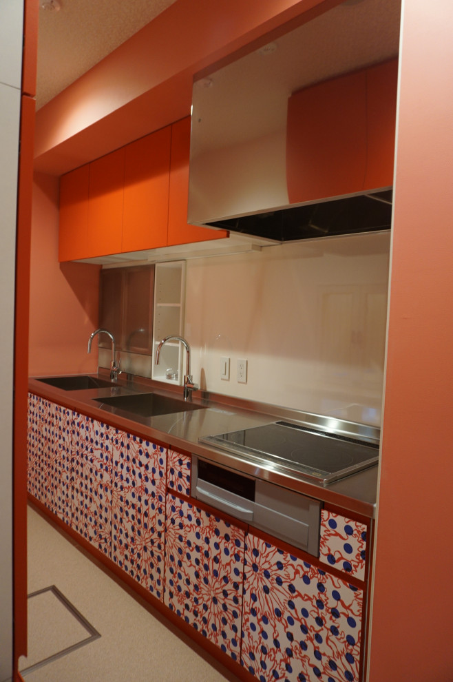 Exotisk inredning av ett avskilt grå linjärt grått kök, med en undermonterad diskho, luckor med profilerade fronter, röda skåp, bänkskiva i rostfritt stål, vitt stänkskydd, glaspanel som stänkskydd, rostfria vitvaror, linoleumgolv, en köksö och beiget golv