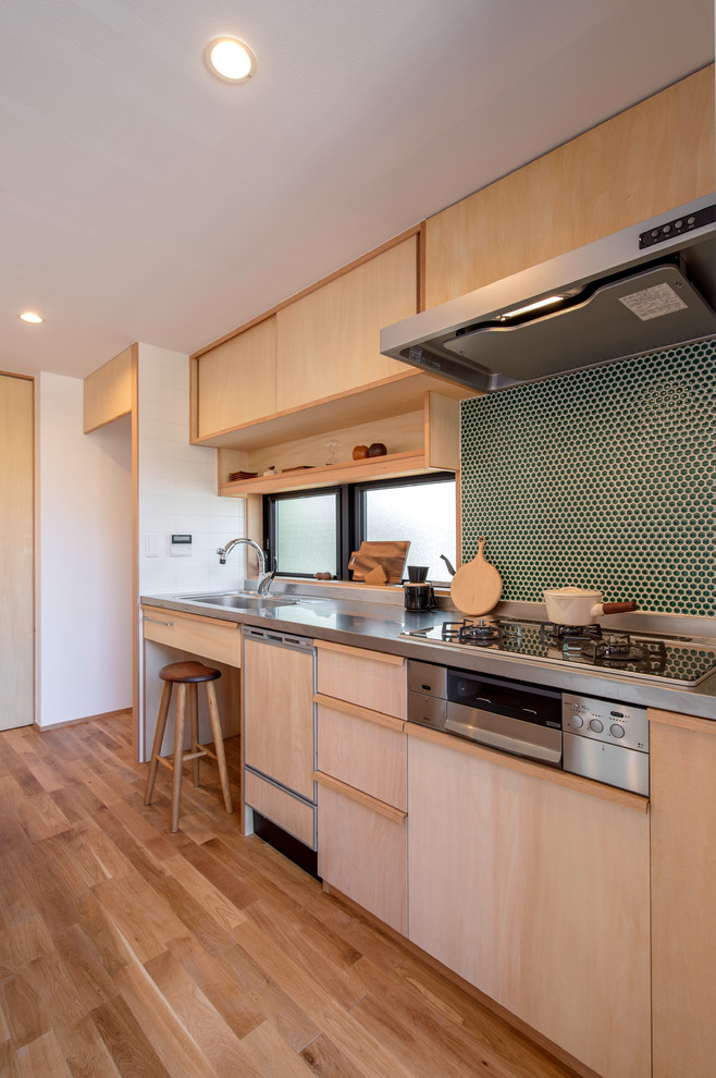 Asiatisk inredning av ett kök, med en integrerad diskho, släta luckor, skåp i ljust trä, bänkskiva i rostfritt stål, mellanmörkt trägolv, en halv köksö och brunt golv