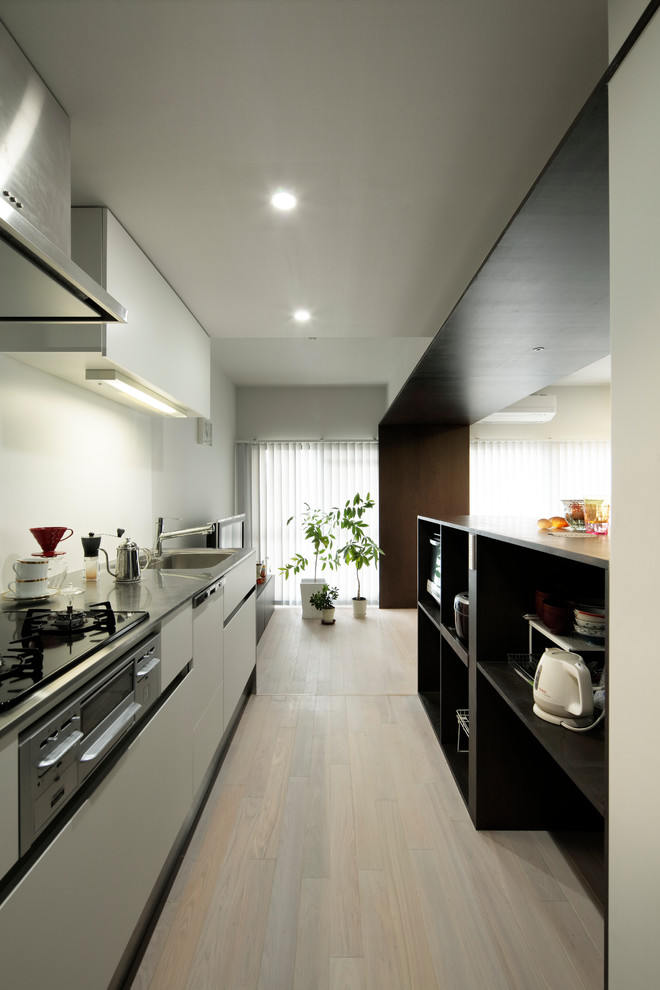 Exempel på ett modernt brun linjärt brunt kök, med öppna hyllor, skåp i mörkt trä, bänkskiva i rostfritt stål, vitt stänkskydd, svarta vitvaror, plywoodgolv, beiget golv och en enkel diskho