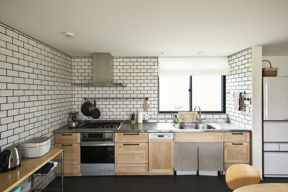 Asiatisk inredning av ett kök, med en enkel diskho, luckor med infälld panel, skåp i ljust trä, bänkskiva i rostfritt stål, vitt stänkskydd, stänkskydd i tunnelbanekakel och svart golv