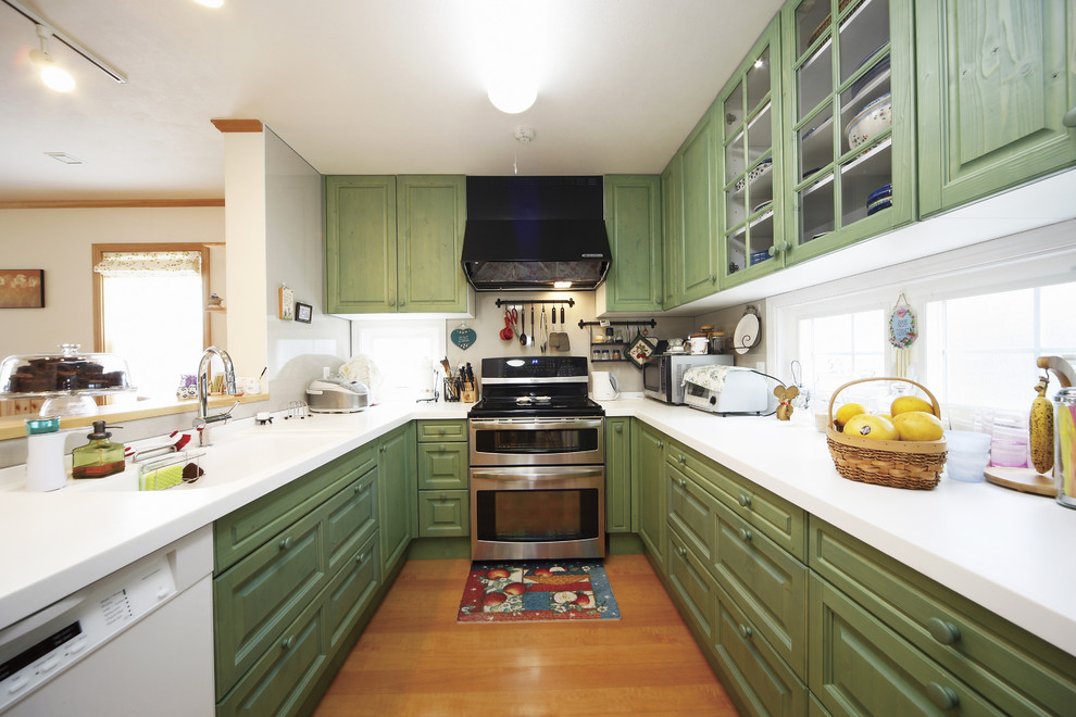 Bild på ett orientaliskt kök, med en integrerad diskho, luckor med infälld panel, gröna skåp, vitt stänkskydd, mellanmörkt trägolv och brunt golv