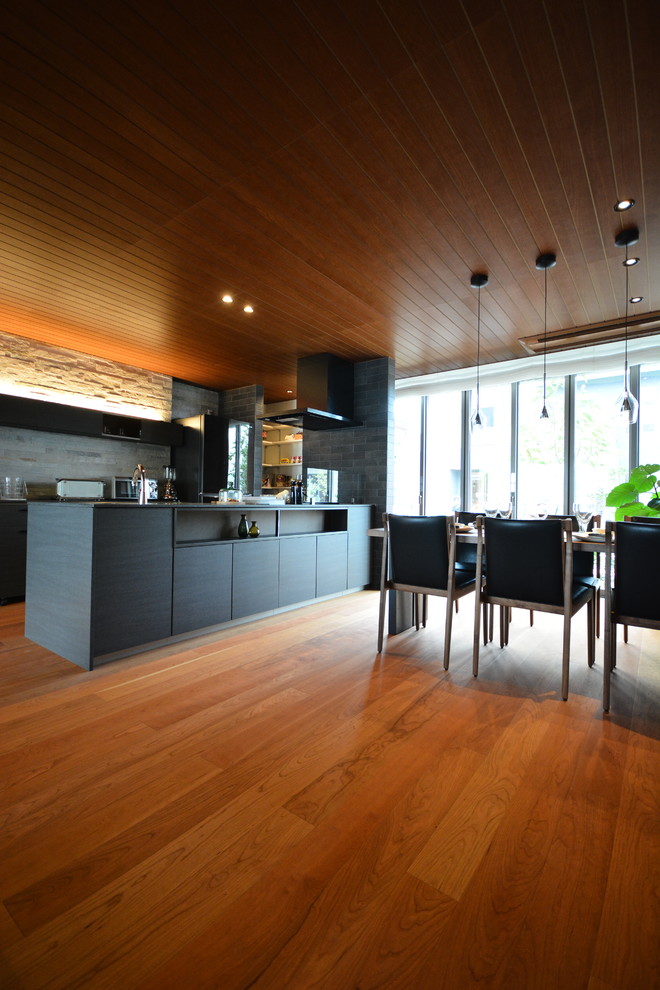 Aménagement d'une cuisine ouverte parallèle moderne avec des portes de placard noires, une crédence noire, un électroménager noir, un sol en contreplaqué, îlot, un sol orange et plan de travail noir.