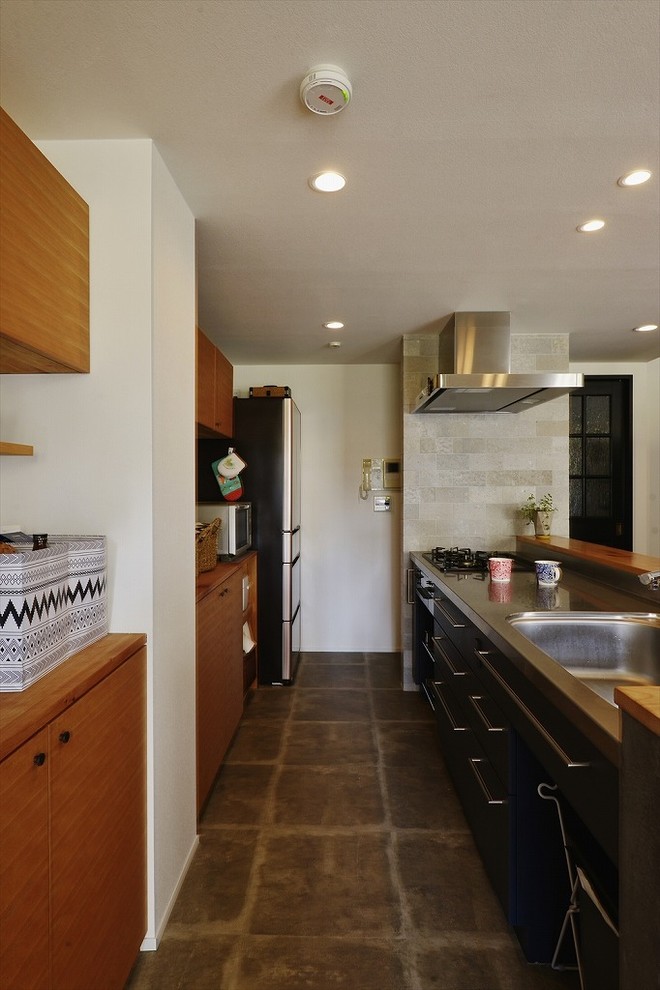 コンテンポラリースタイルのおしゃれなキッチン (シングルシンク、フラットパネル扉のキャビネット、中間色木目調キャビネット、ステンレスカウンター、シルバーの調理設備、グレーの床、茶色いキッチンカウンター) の写真