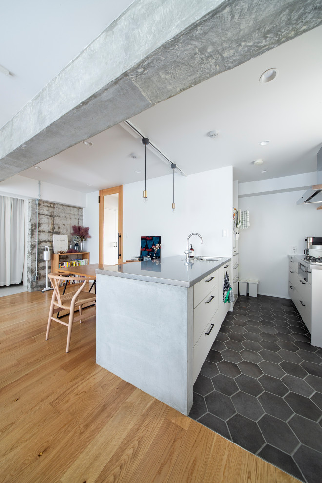 Example of a minimalist ceramic tile, gray floor and exposed beam open concept kitchen design in Osaka with an integrated sink, beaded inset cabinets, white cabinets, stainless steel countertops, white backsplash, white appliances and an island