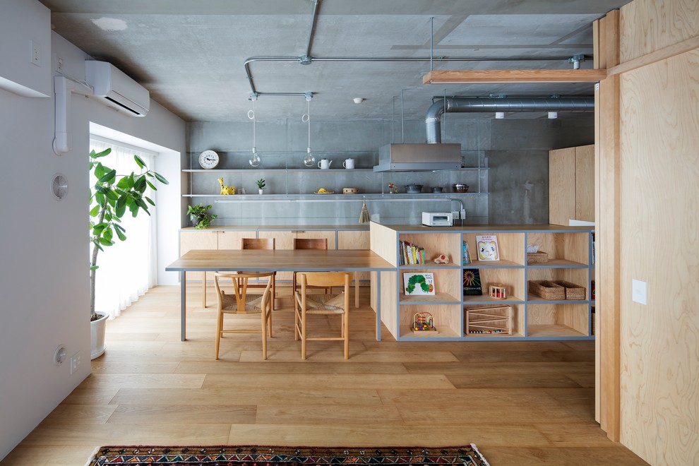 Foto på ett industriellt kök, med släta luckor, skåp i ljust trä, träbänkskiva, grått stänkskydd, ljust trägolv, en köksö och brunt golv