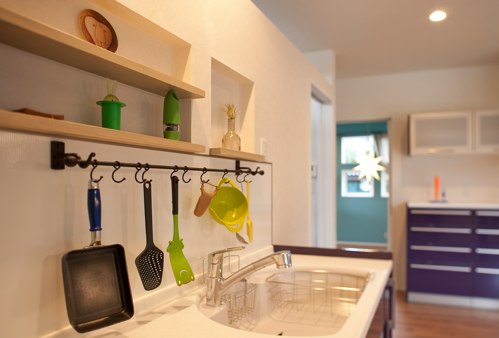 Стильный дизайн: прямая кухня-гостиная с монолитной мойкой, фиолетовыми фасадами, столешницей из акрилового камня, техникой из нержавеющей стали, полом из фанеры, островом и коричневым полом - последний тренд